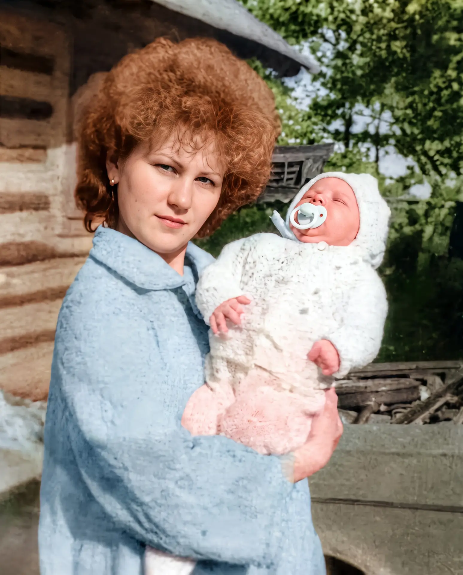 Restored and colourised photograph of a young mother in a blue coat holding a newborn in a knitted bonnet