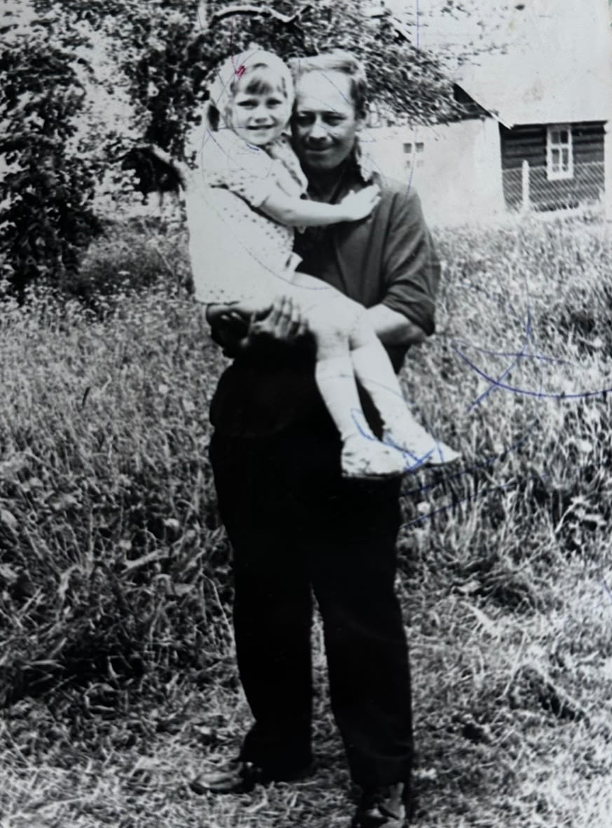 Original black and white photograph of a man holding a small girl outside a village house