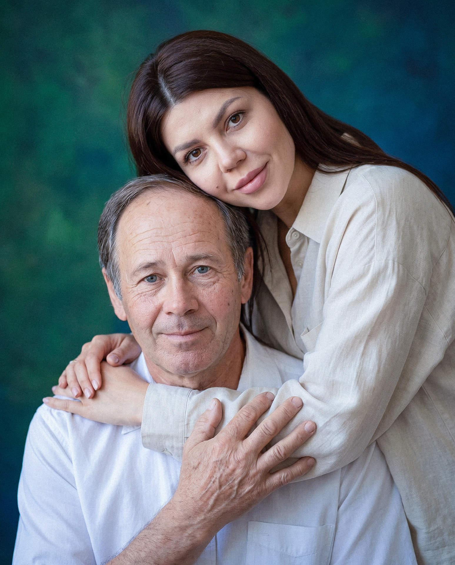 Fine art portrait of a father and his adult daughter embracing against a deep green backdrop