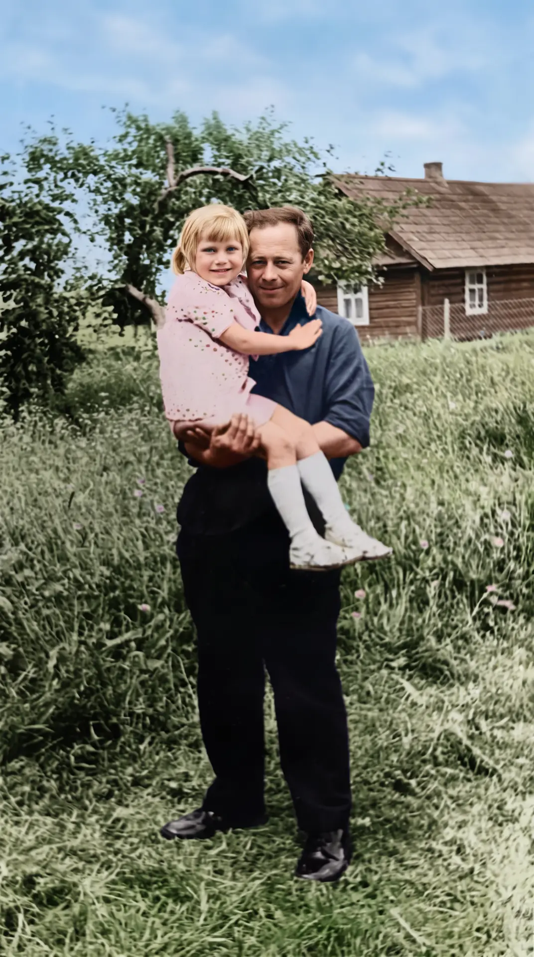 Restored and colourised photograph of a man holding a small girl in a summer meadow
