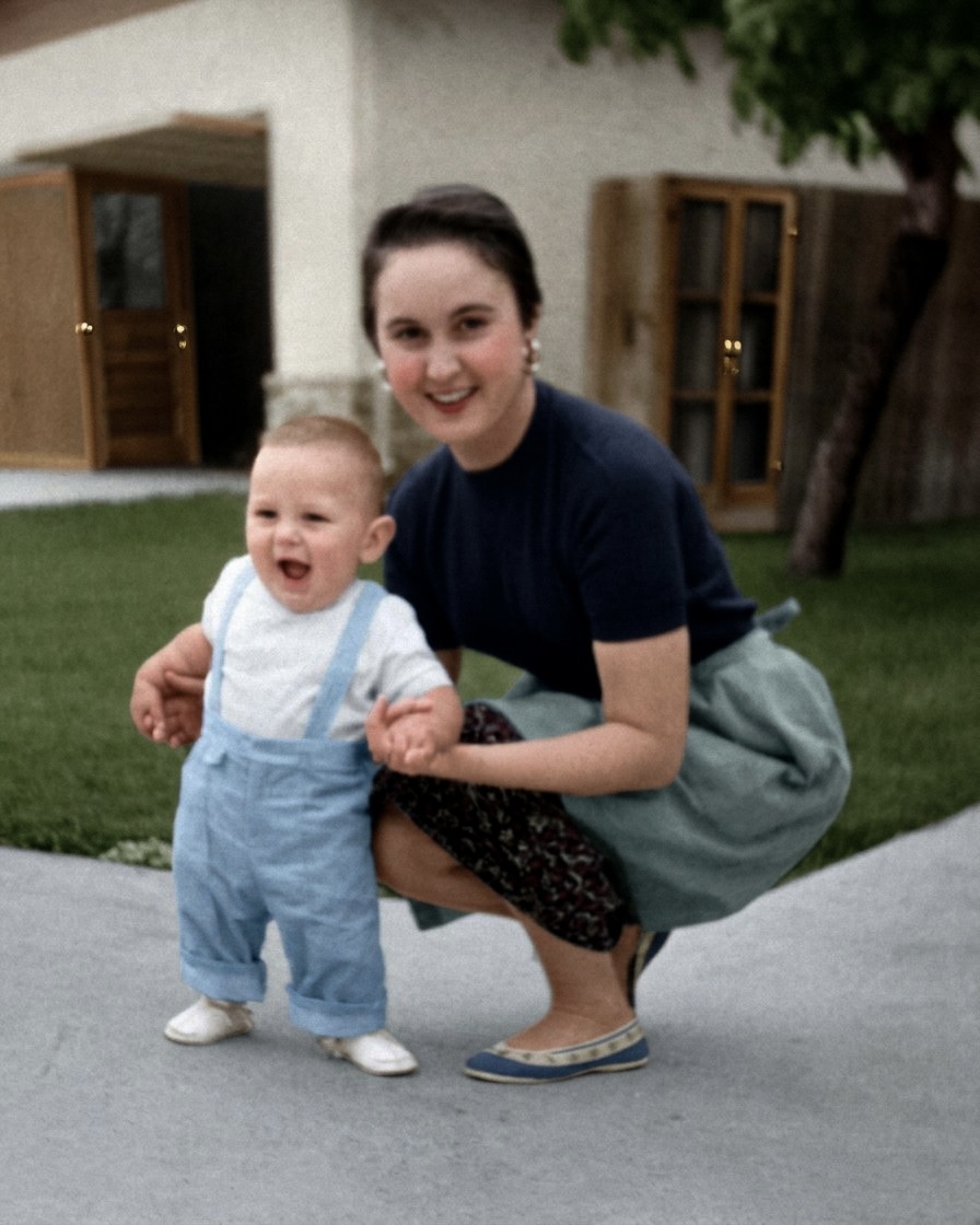 The same photograph restored and colourised — navy top, sage skirt, pale blue dungarees, green lawn and a white house behind