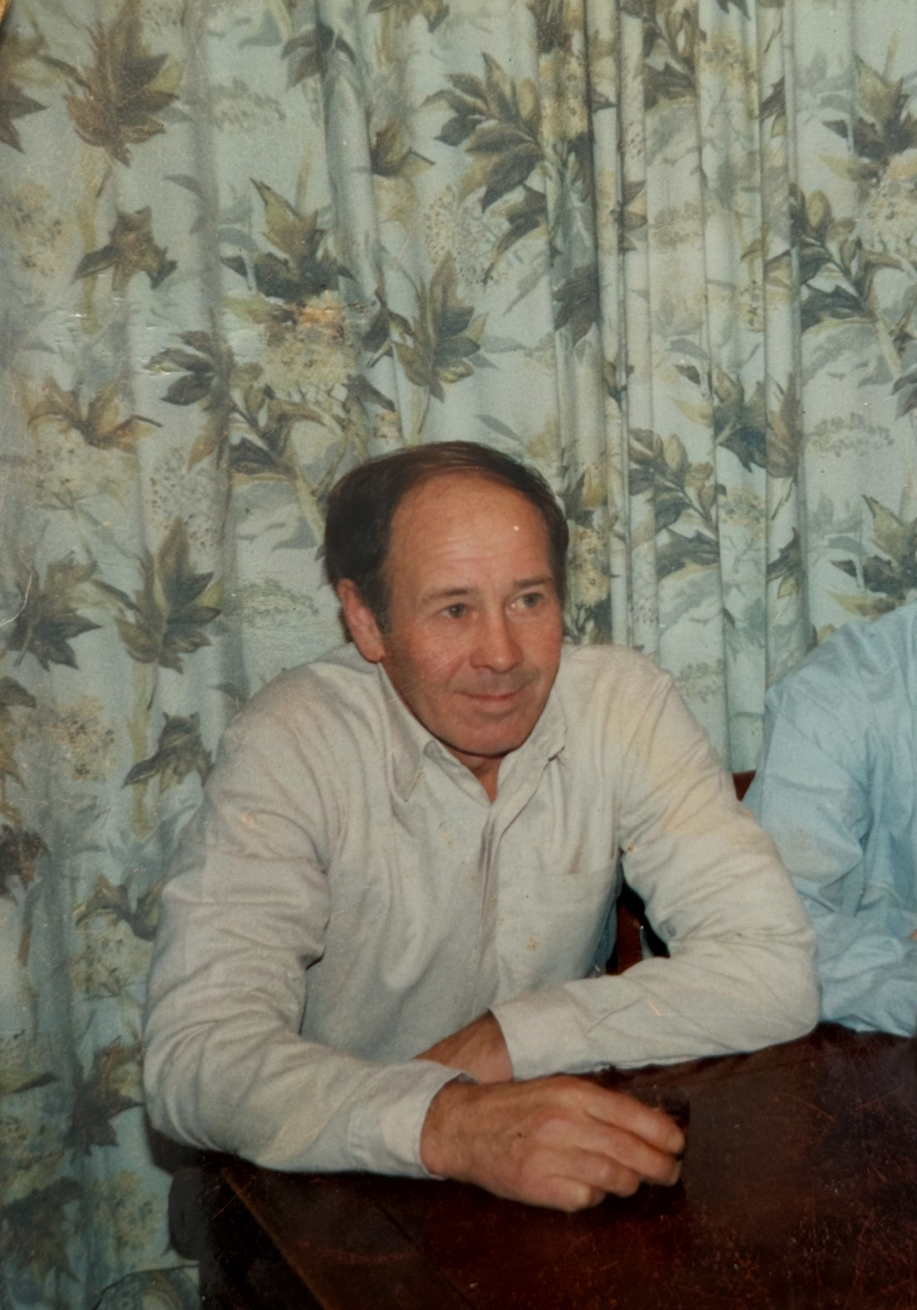 Old family photograph of a man seated at a table in front of patterned curtains